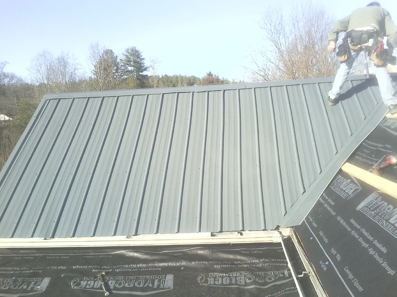 Crew installing dark green standing seam panels over synthetic underlayment in Little Ferry