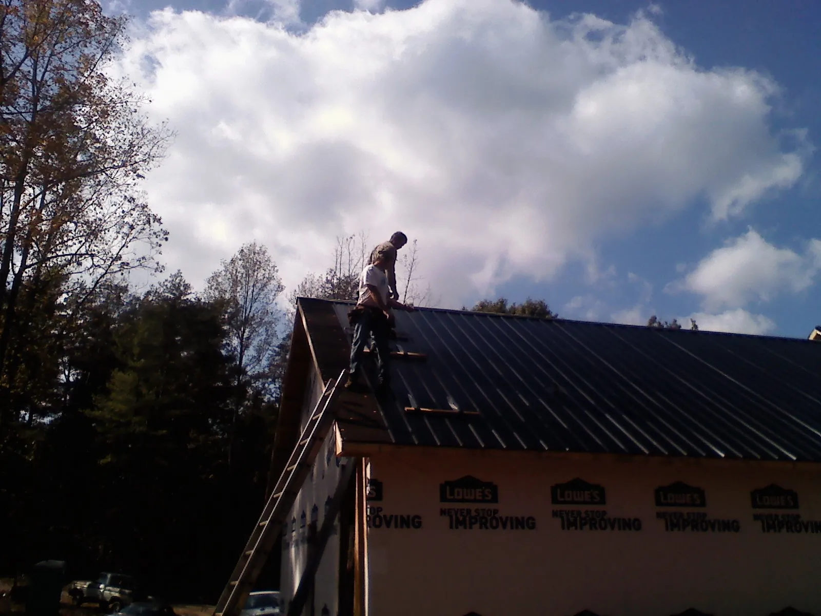 Roofer fastening dark metal panels high against a cloudy sky, from a Roof Inspection job in Little Ferry