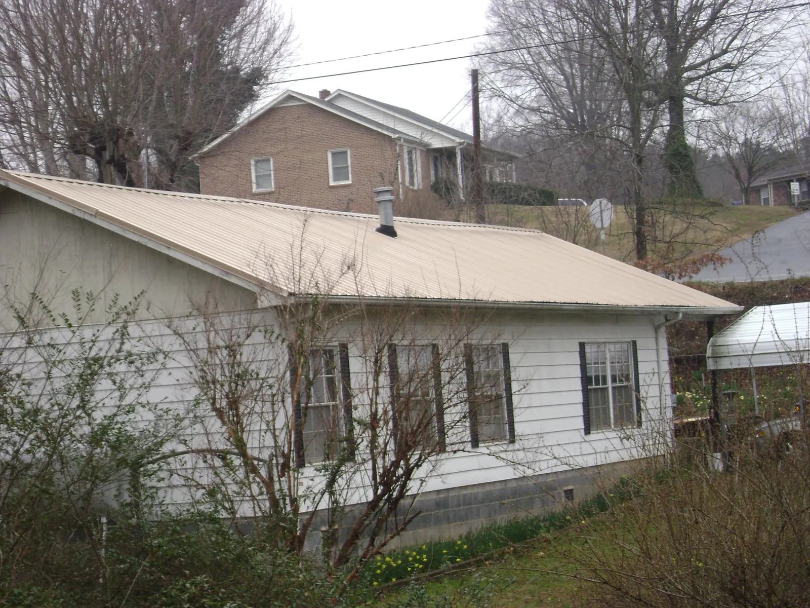 Tan metal roof on a white sided house set into a hillside — Commercial Roofing by Roofing Brothers in Little Ferry